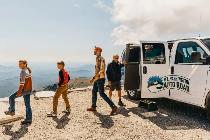 a group of people exiting a tour van on top of a mountain