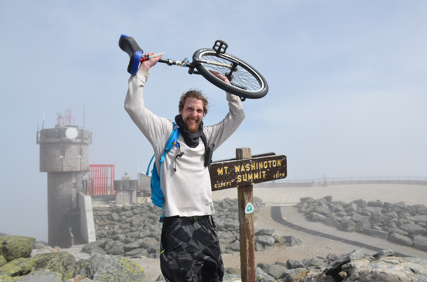 AltonWeagleDay_web a person holds a unicycle next to the Mt.Washington Summit Sign